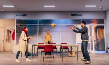 a stage set with a woman and a man throw a ball in a classroom while another woman looks on