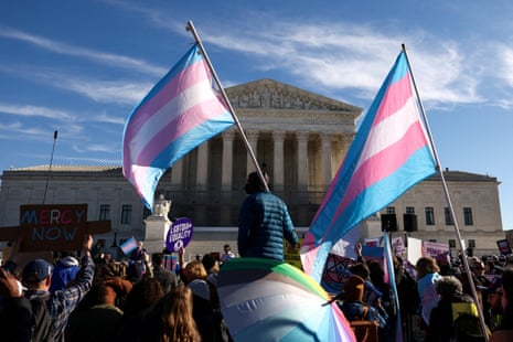 People hold blue, pink and white trans pride flags outside white building
