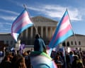 People hold blue, pink and white trans pride flags outside white building