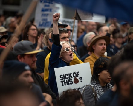 A striking council worker raises her fist, holding a "Sick of this?" sign amid the crowd