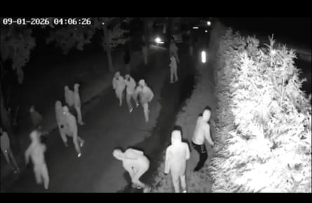 Grainy black and white footage of at least 15 masked men in hoodies