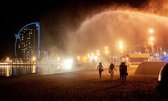 People walk under a spray of water on the seafront at La Barceloneta at night-time