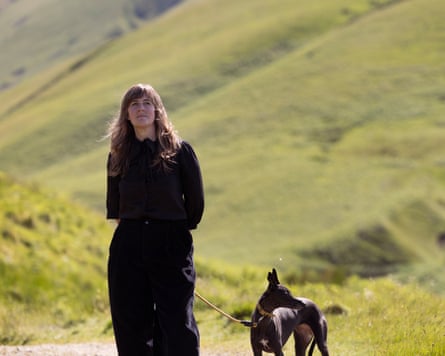 A woman dressed in black and a whippet are shown in a green valley.