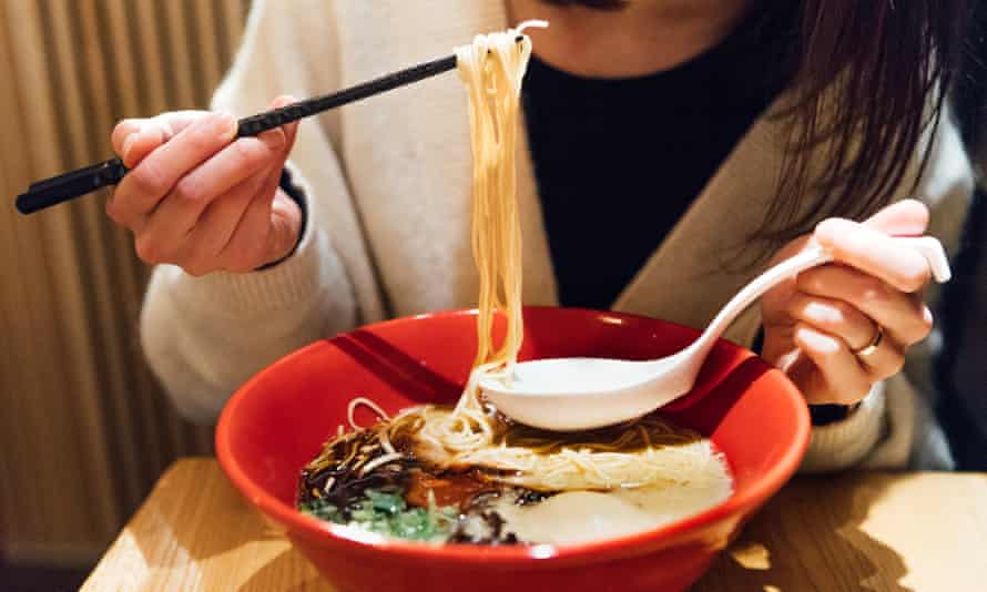 Young woman eating a bowl of ramen on a wooden table 