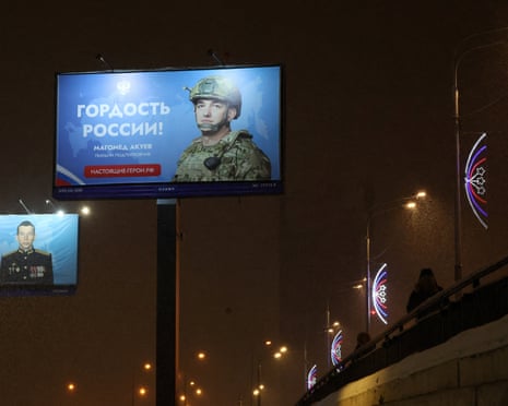 Billboards showing Russian soldiers in Moscow in the snow lit by lamplight at night