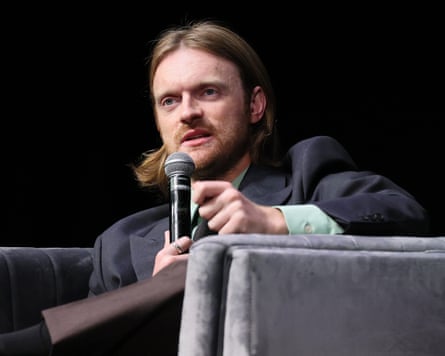 A seated Finneas holds a microphone