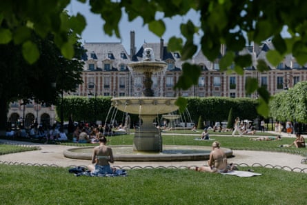 People sit on blankets on the grass near a fountain in the elegant square