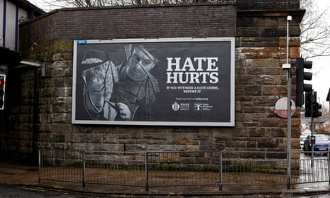 The billboard against a stone wall on a street corner reads: 'Hate hurts: if you witness a hate crime, report it. Police Scotland'