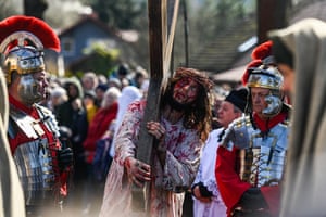 Man carries large cross surrounded by others in costume