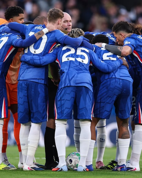 Chelsea players in blue kit huddle around Referee Paul Tierney on the pitch