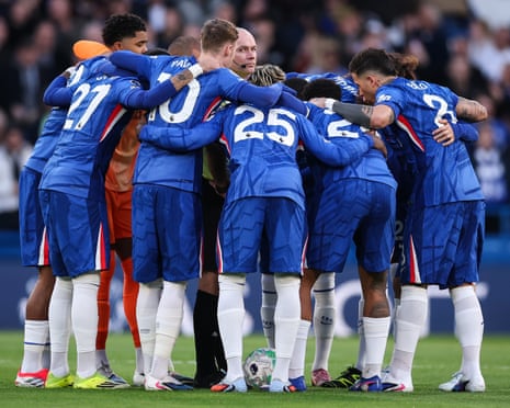Chelsea players in blue kit huddle around Referee Paul Tierney on the pitch