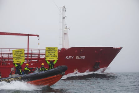 Greenpeace activists in a small boat hold up signs to the camera as they intercept a tanker