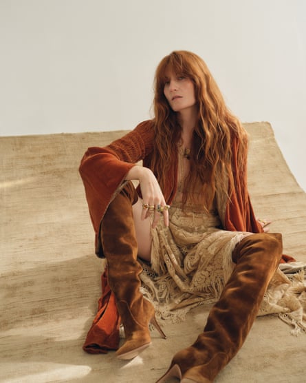 Florence Welch sitting on the ground, wearing a flowing rust-coloured outfit and long, brown boots