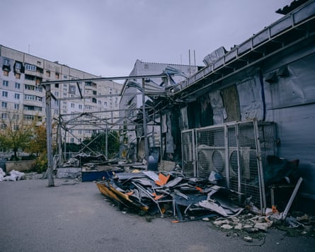 A damaged building with piles of debris in the yard outside. Tower blocks can be seen on a neighbouring street