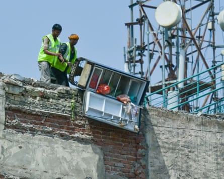 Two mention in hi-vis vests tip the contents of a fridge over the edge of a building marked for demolition in Delhi