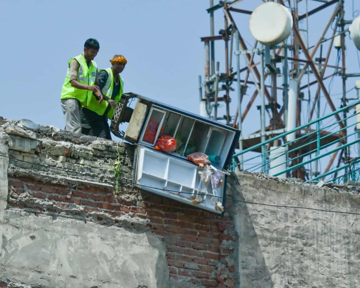Two mention in hi-vis vests tip the contents of a fridge over the edge of a building marked for demolition in Delhi