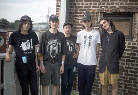 The band standing outside with four of them wearing graphic T-shirts and baseball caps while a fifth, Colin Caulfield, wears his cap back to front with a black linen shirt