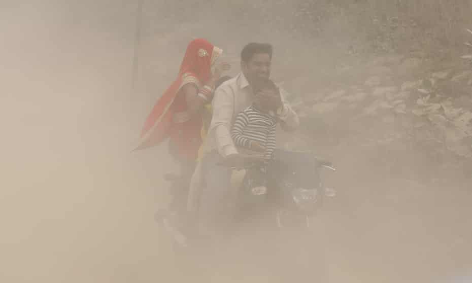 An Indian man and his family ride a bike during heavy dust and smog in Delhi.