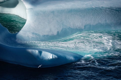 The curved shape of an iceberg makes an abstract impression as the ocean is visible through gaps in its structure