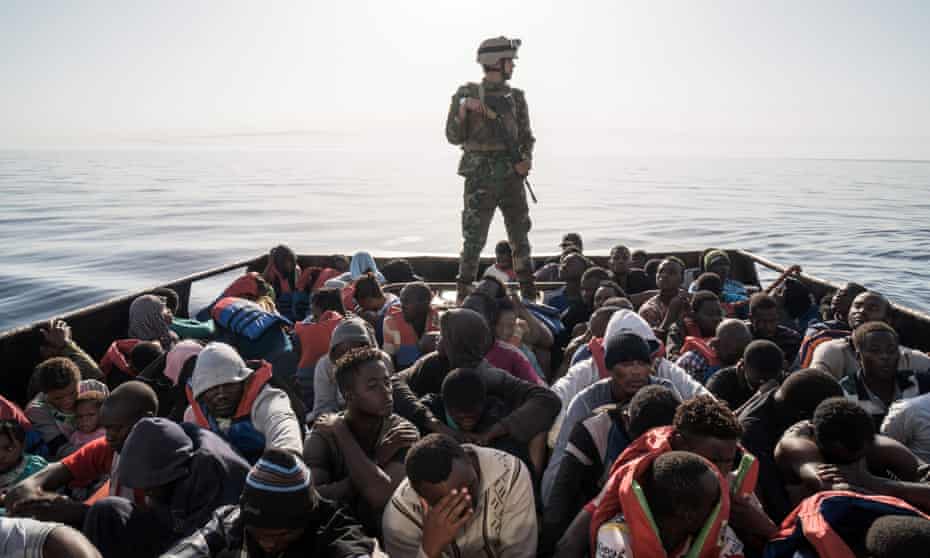 A Libyan coastguardsman stands on a boat carrying  migrants off the coastal town of Zawiyah