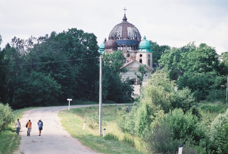 Three people walk along an empty road with a Russian church in the background.