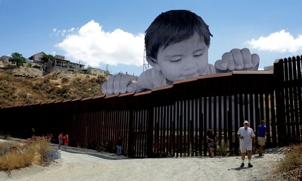 An art installation created by French artist JR rises above and appears to peek over the border wall that bisects Tecate, Mexico and Tecate, California, USA.
