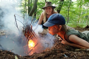 A boy breathes life into a campfire in a woodland clearing as his teacher looks on, 2007