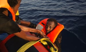 A migrant from Eritrea is helped after jumping into the water from a crowded wooden boat.