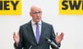 John Swinney makes an open-handed gesture as he stands in front of a microphone