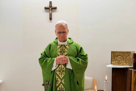 Pope Leo XIV, in green vestments, stands with hands clasped in prayer before a crucifix