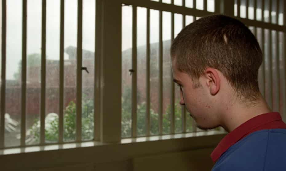 Young man in young offender institution looking out of barred window