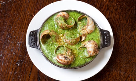 Six snails in their shells in a dish full to the brim with green garlic butter