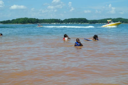 kids swimming in a lake as a boat drives by behind them