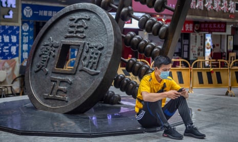 A man uses his cellphone as he sits next to a sculpture representing the Chinese yuan in Guangzhou, Guangdong province.