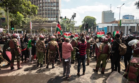 Police stand in a line to stop protesters advancing. Protesters hold Kenyan flags in the air