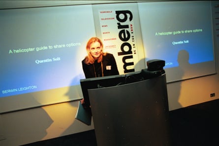Julie Meyer wearing a black blazer, standing at a podium in front of a large screen