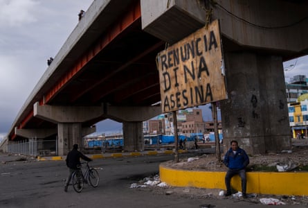 A man sits next to a sign that reads in Spanish ‘Dina Murderer, Resign,’ in Juliaca, a reference to Peru’s president Dina Boluarte.