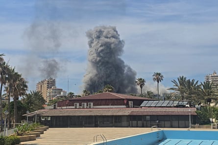Smoke rises from a site behind buildings and an empty swimming pool in the foreground