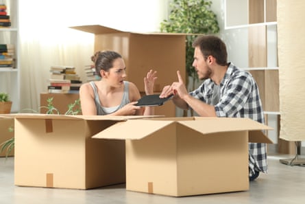 A couple sit in front of two cardboard boxes as they fight over an electronic tablet.