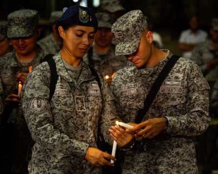 A man in camouflage fatigues with air force insignia lights a candle next to a woman in similar uniform