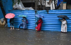 Mumbai, India. Women holding umbrellas are seen crossing a flooded street amidst heavy rain in the city
