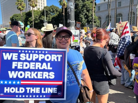 woman smiling outside at protest, holding a sign saying ‘we support federal workers / hold the line’