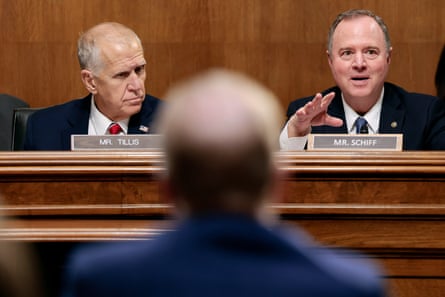 Two men in suits on a dais, one speaking.