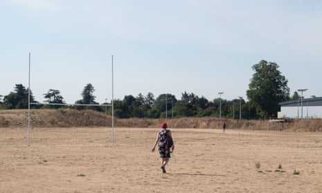 A woman walks across parched grass on a rugby pitch  in Maidenhead, Berkshire