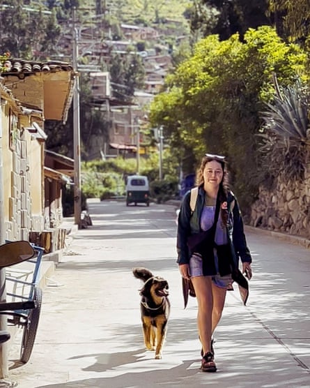 They walk together us a hilly road, with buildings on one side and a stone wall covered in shrubbery on the other