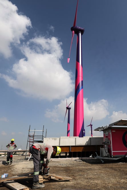 A man bends down with two wind turbines behind him