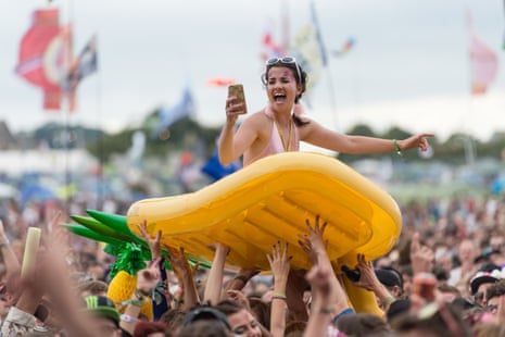 A festival goer is carried above the heads of others on an inflatable bed in the shape of a pineapple as Glass Animals perform on the Other Stage