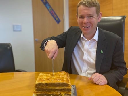 Man in a suit looking at the camera, with a knife poised above sausage roll cake