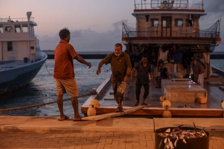 A group of men disembark a fishing boat via a wooden plank at sunset
