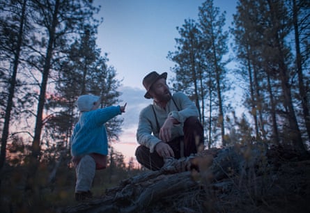 In woods an infant points while a crouching Joel Edgerton looks in the direction she’s pointing at